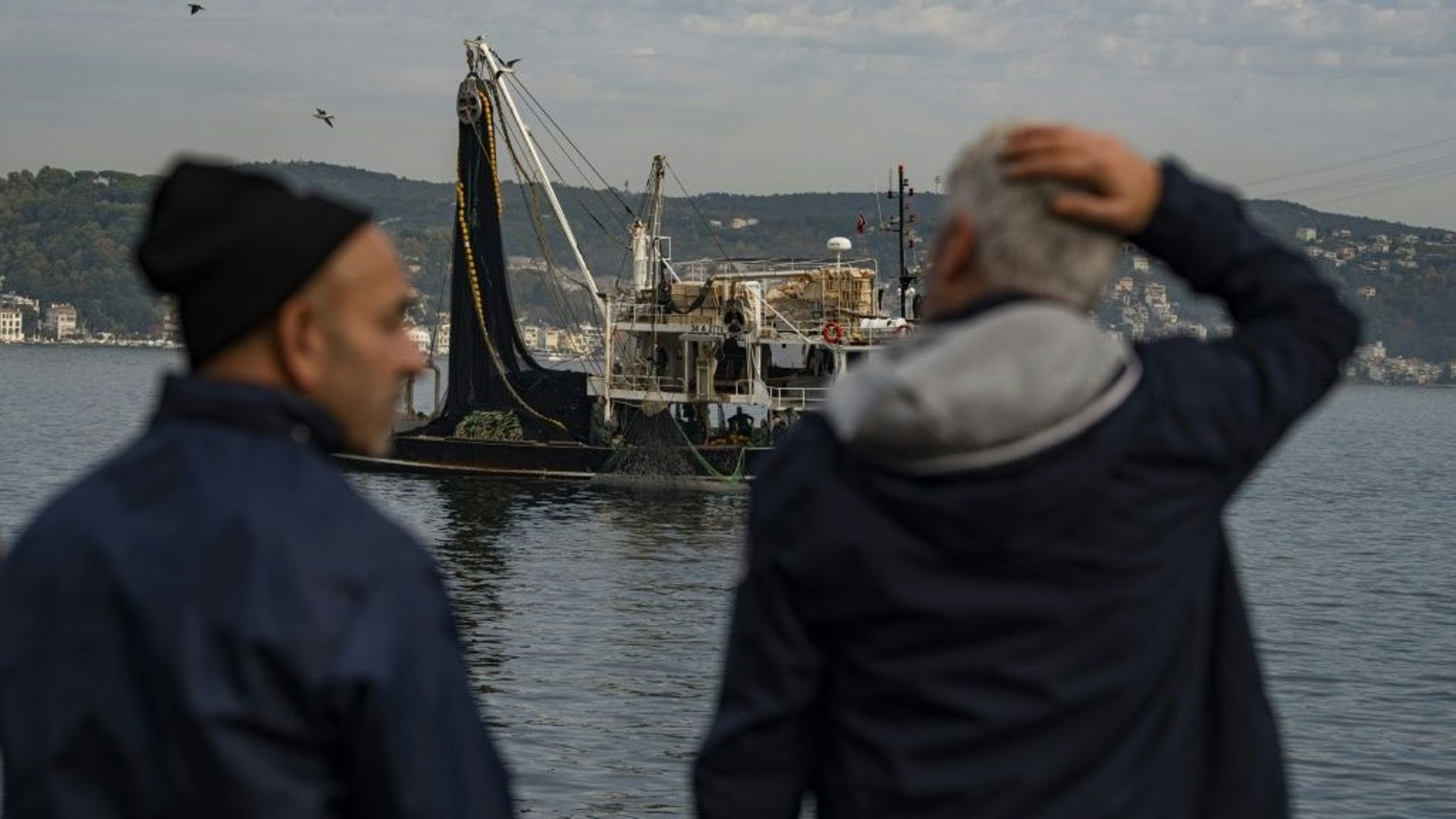 Des pêcheurs sur la rive du Bosphore où un senneur remonte son immense filet au moyen d'un treuil, le 6 novembre 2022, à Istanbul.