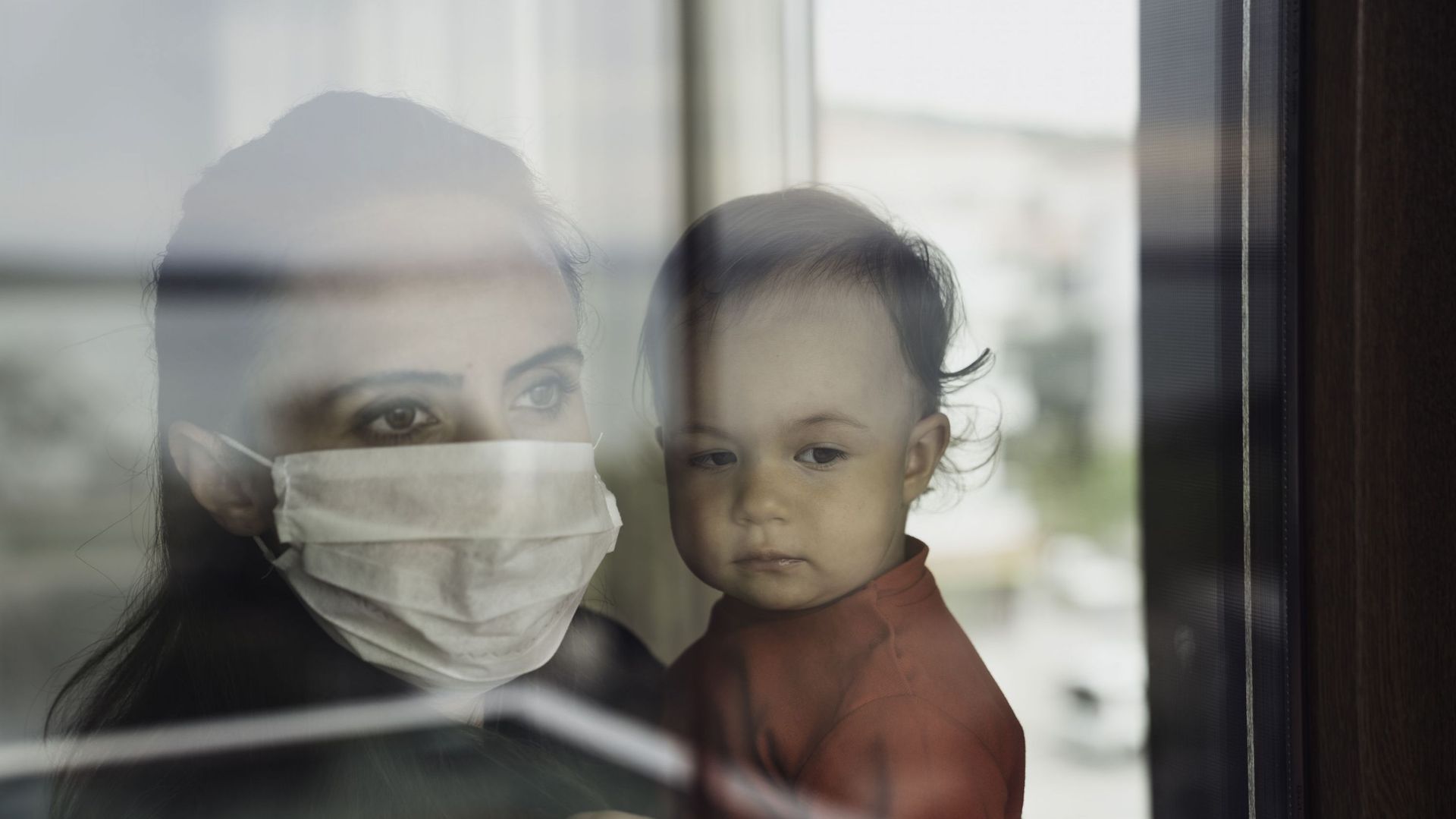 Cute little girl and Mother whit protective mask standing next to the window