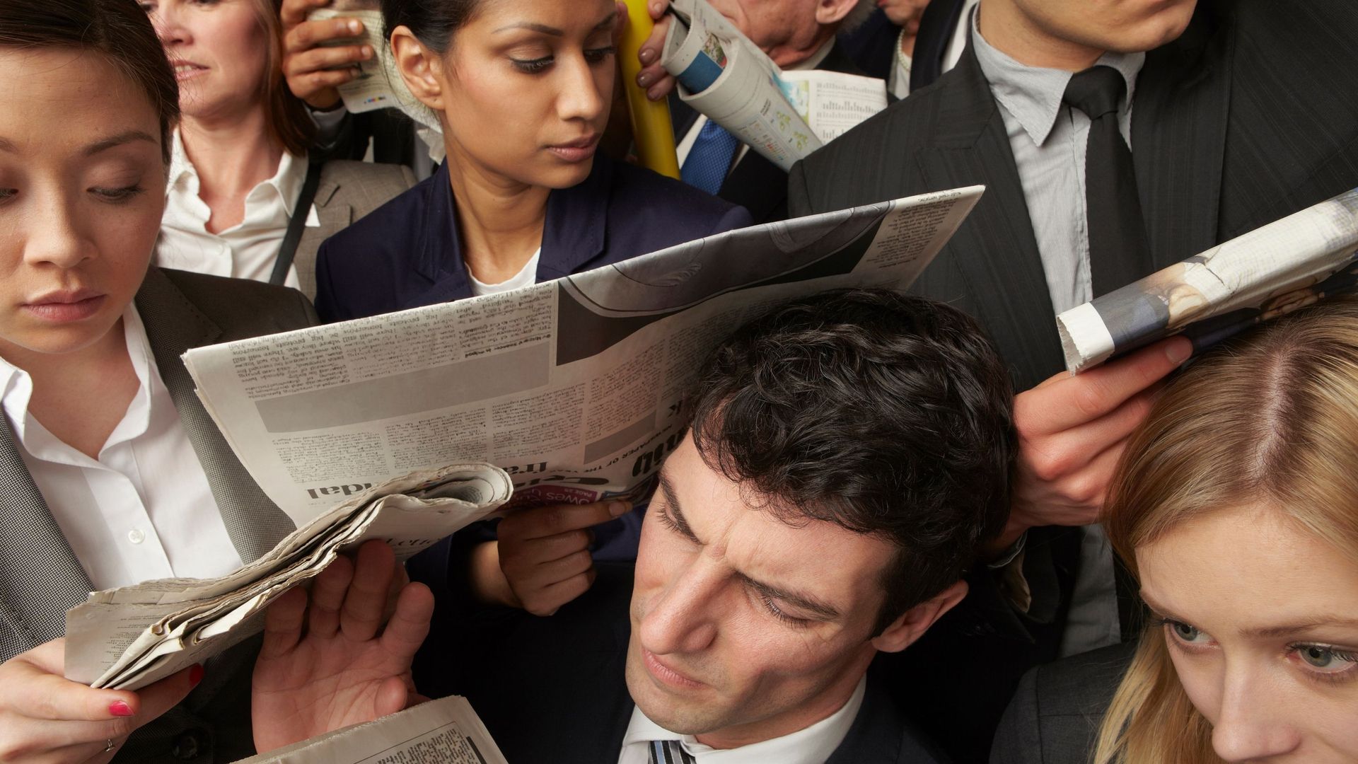 Businesspeople reading newspapers on crowded train