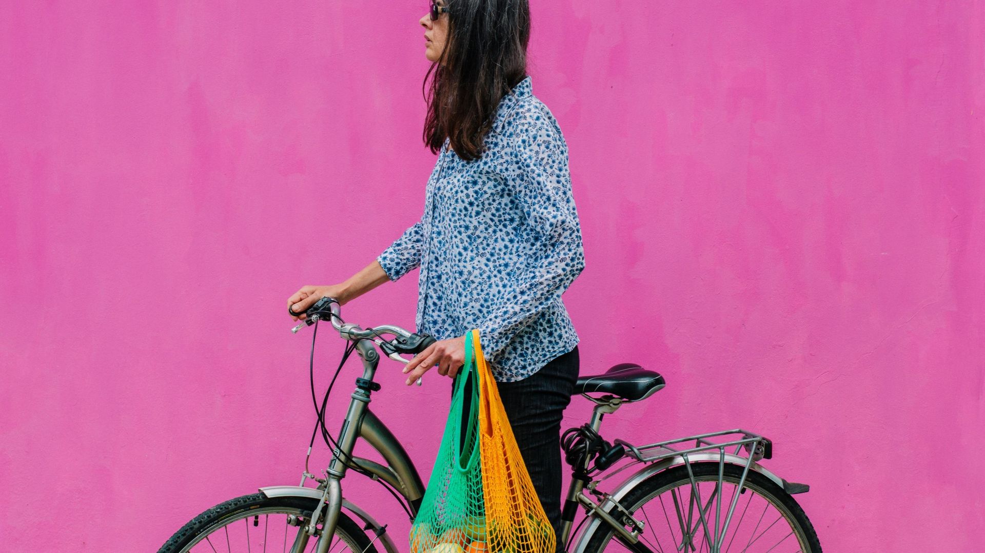 woman with classic dutch bike with reusable bags with a sustainable purchase on pink background