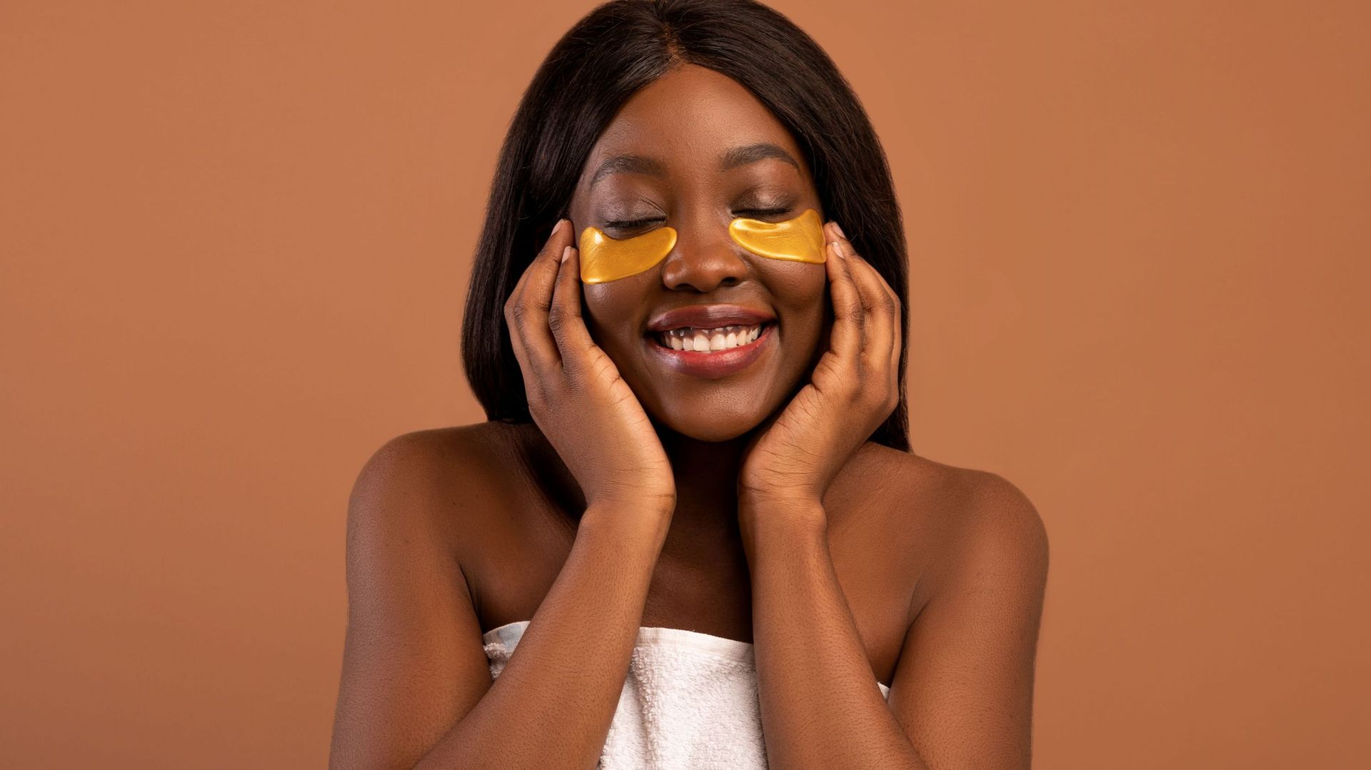 Closeup of joyful black lady applying golden eye patches