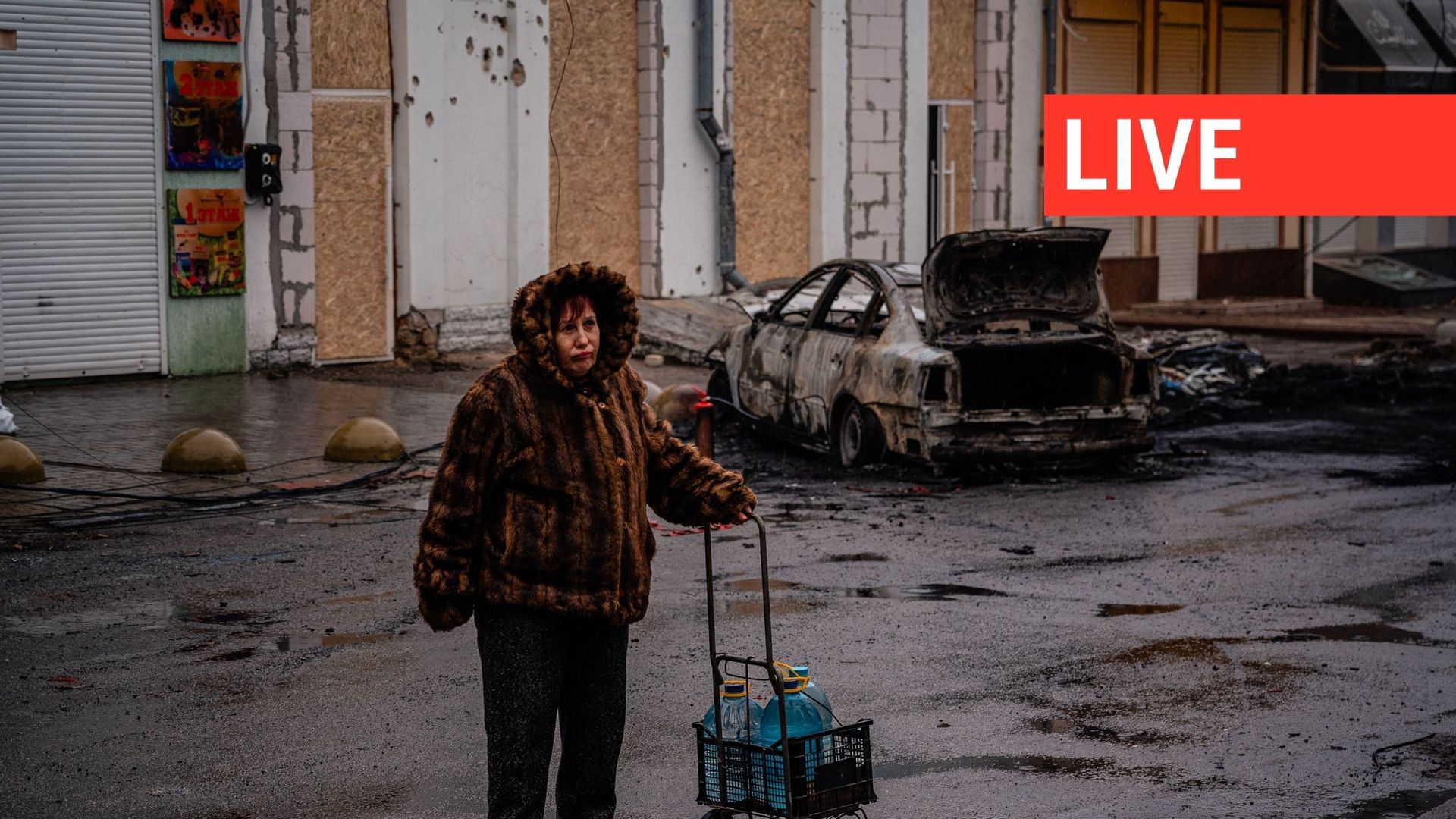Une femme tient un chariot avec des bouteilles d'eau et regarde les conséquences du bombardement de la ville ukrainienne de Kherson, le 25 décembre 2022, lors de l'invasion russe de l'Ukraine.