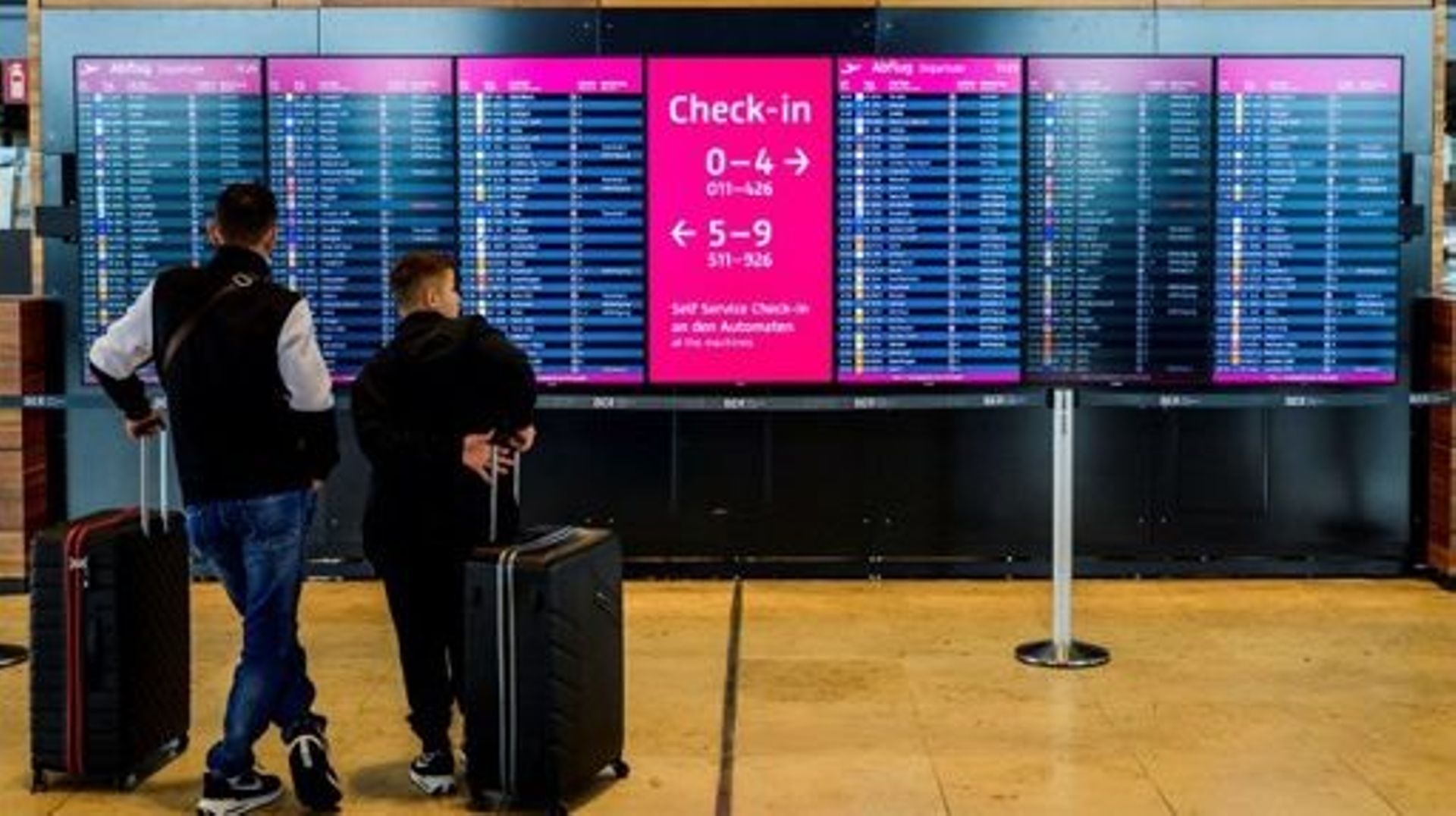 Passengers check out a digital billboard displaying flight information at Berlin Brandenburg International airport's terminal 1 near Schoenefeld on July 7, 2022, on the first day of the school holidays for the state of Berlin.   John MACDOUGALL / AFP