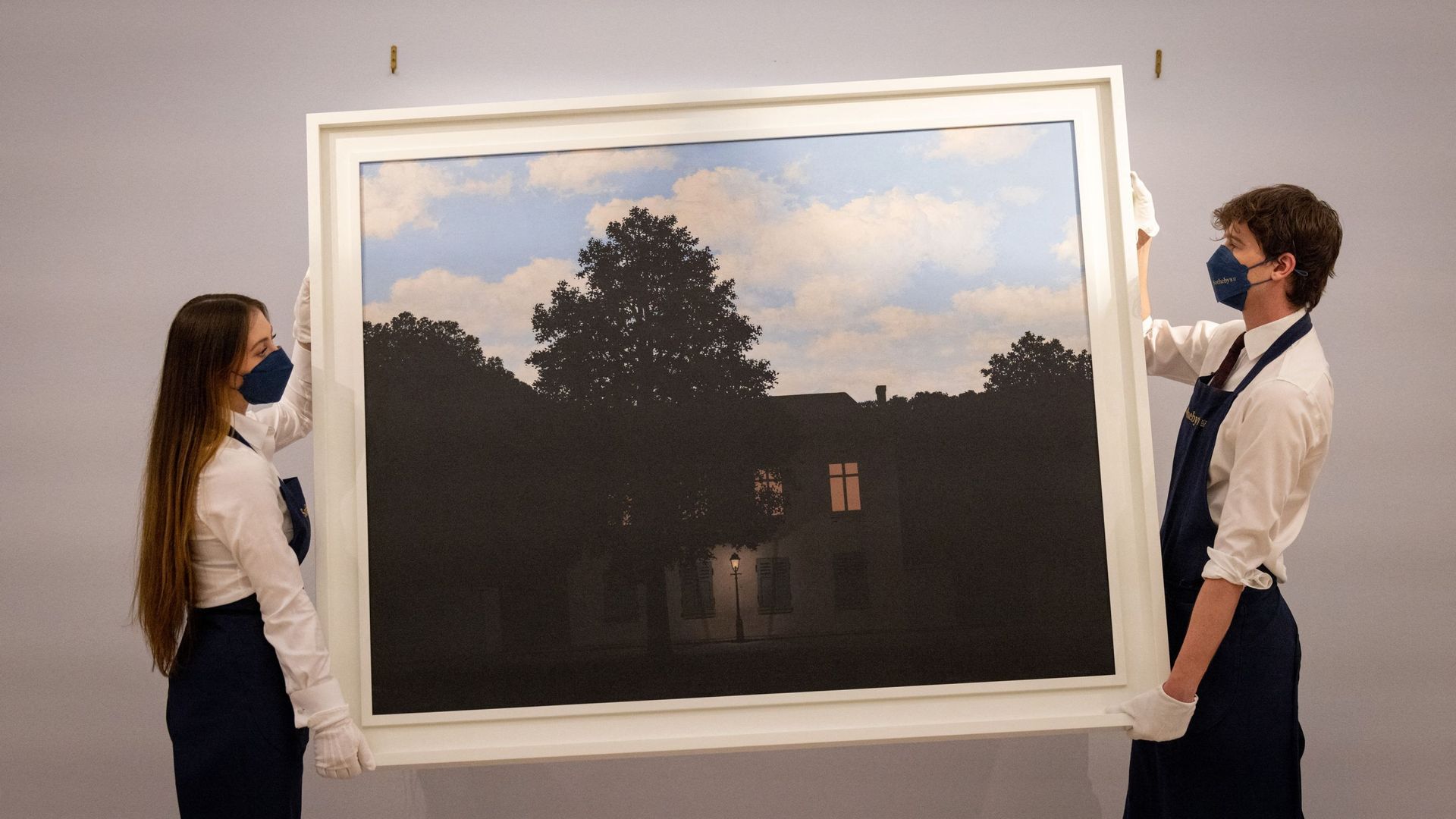 Les assistants de la galerie posent avec une œuvre intitulée "L’empire des lumières" par l’artiste belge Rene Magritte, lors d’une séance photo en amont d’une vente d’Art Moderne et Contemporain, chez Sotheby’s.