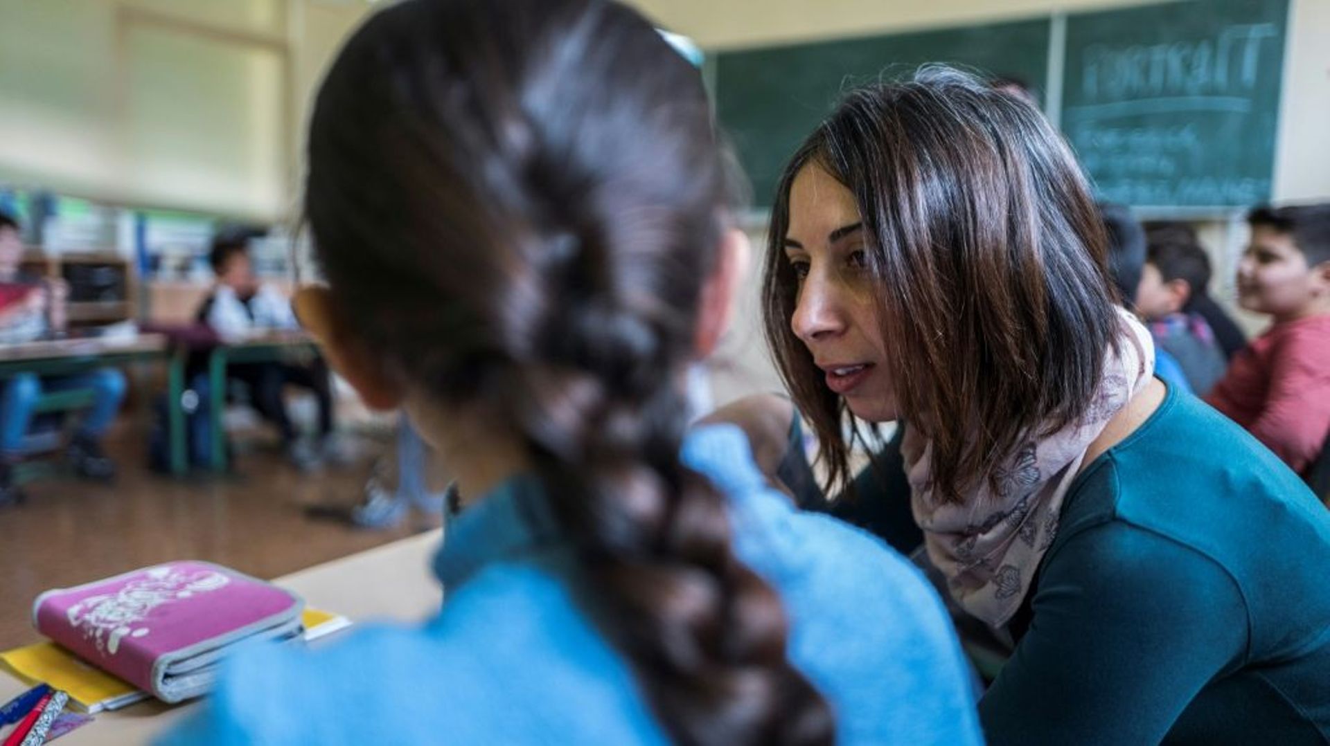 La jeune réfugiée Yasmine, avec sa longue tresse, se fait aider par l'assistante syrienne Hend Al Khabbaz, formée depuis peu à l'enseignement allemand et qui parle l'arabe comme elle. A Fürstenwalde, le 19 janvier 2018