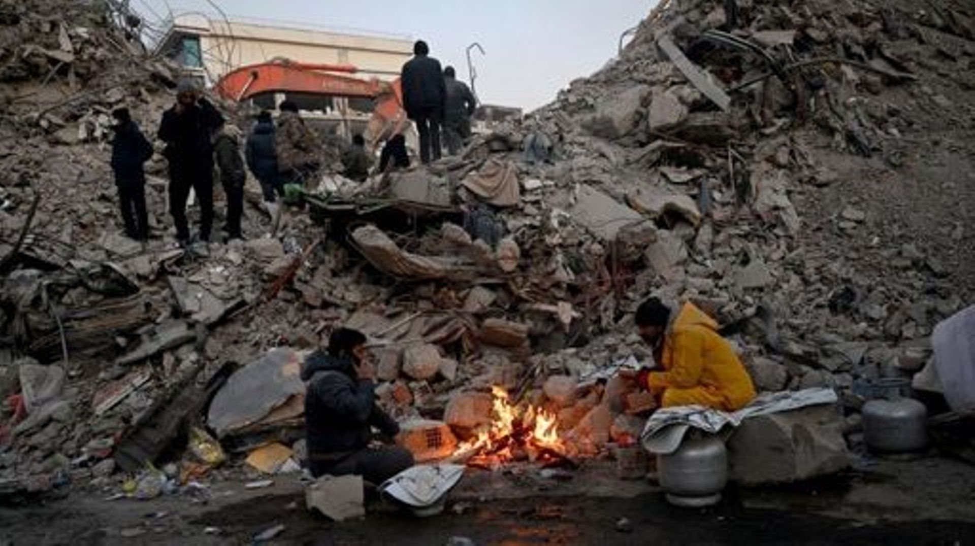 Relatives warm up around a fire in front of rubble of collapsed buildings as rescue teams continue to search victims and survivors, after a 7.8 magnitude earthquake struck the border region of Turkey and Syria earlier in the week, in Kahramanmaras on Febr