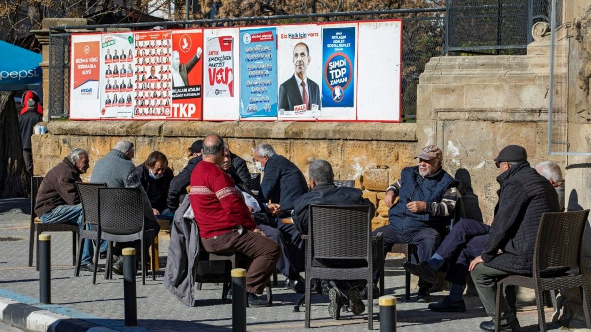Des hommes à la terrasse d’un café à côté d’affiches électorales pour les législatives, le 20 janvier 2022 à Nicosie, dans la partie de la République turque de Chypre-Nord (RTCN).
