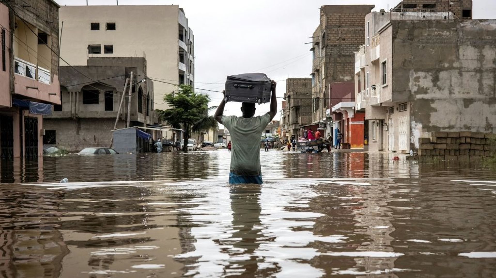 Un homme porte une valise sur sa tête en traversant une rue inondée de Dakar, au Sénégal, le 20 août 2021