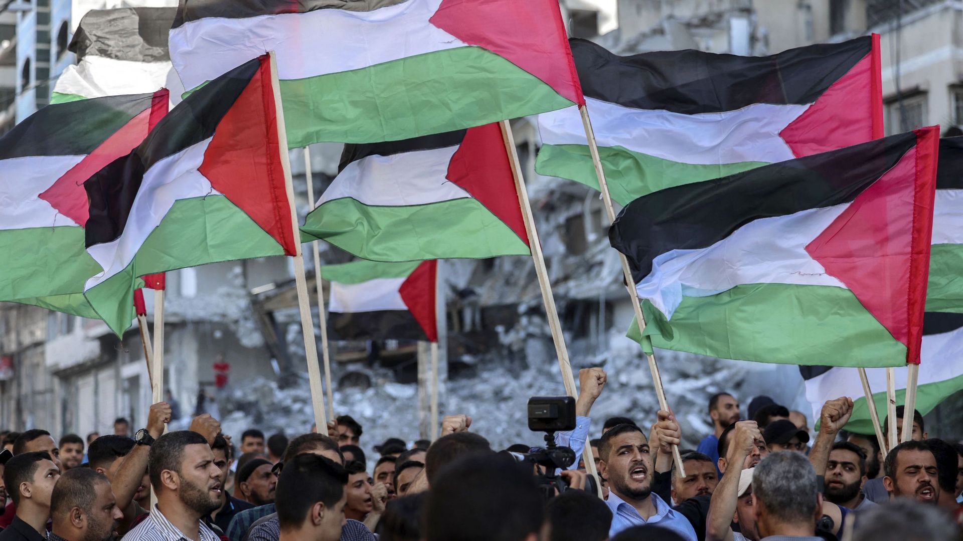 Des Palestiniens brandissent des drapeaux nationaux en passant devant des bâtiments détruits par des frappes aériennes israéliennes dans la ville de Gaza, le 15 juin 2021, lors d’une manifestation contre la Marche des drapeaux ultranationaliste israélienn