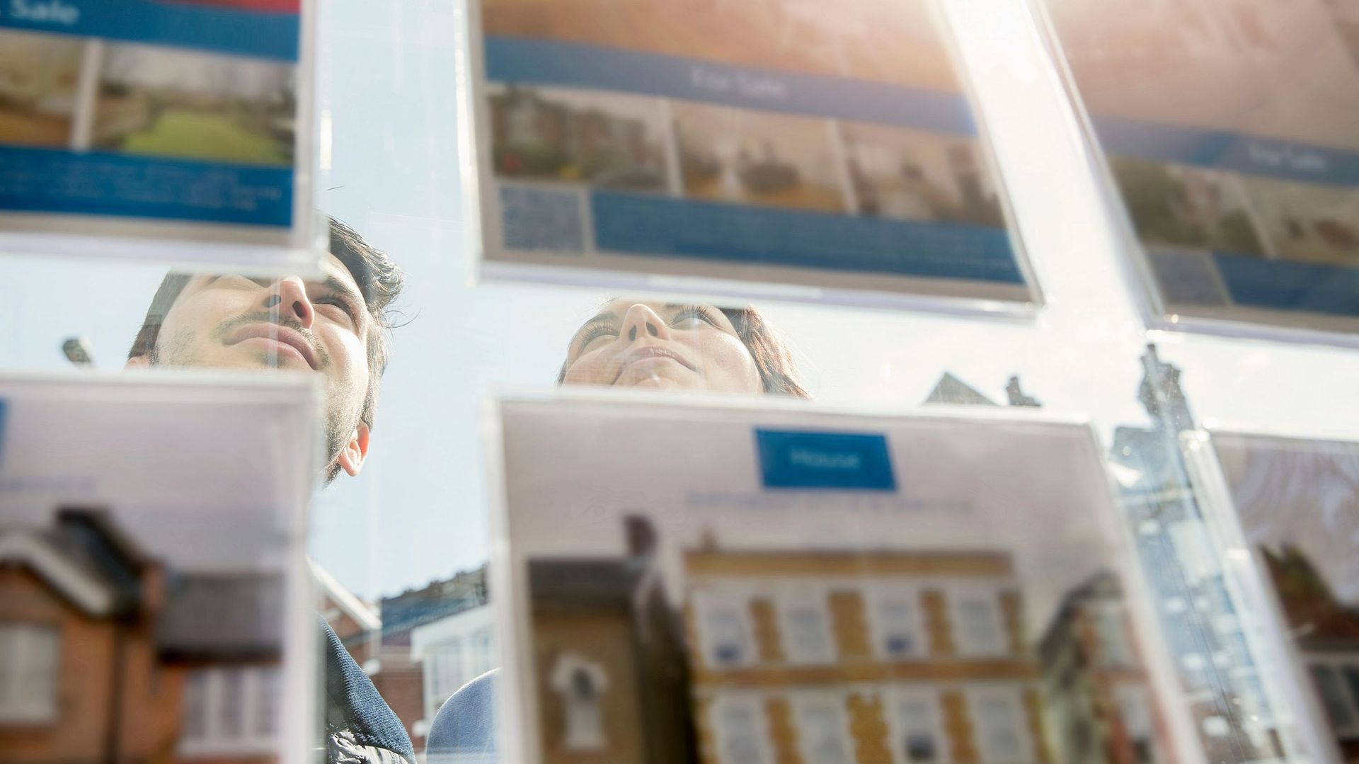 Couple looking at display of advertisements in estate agent window