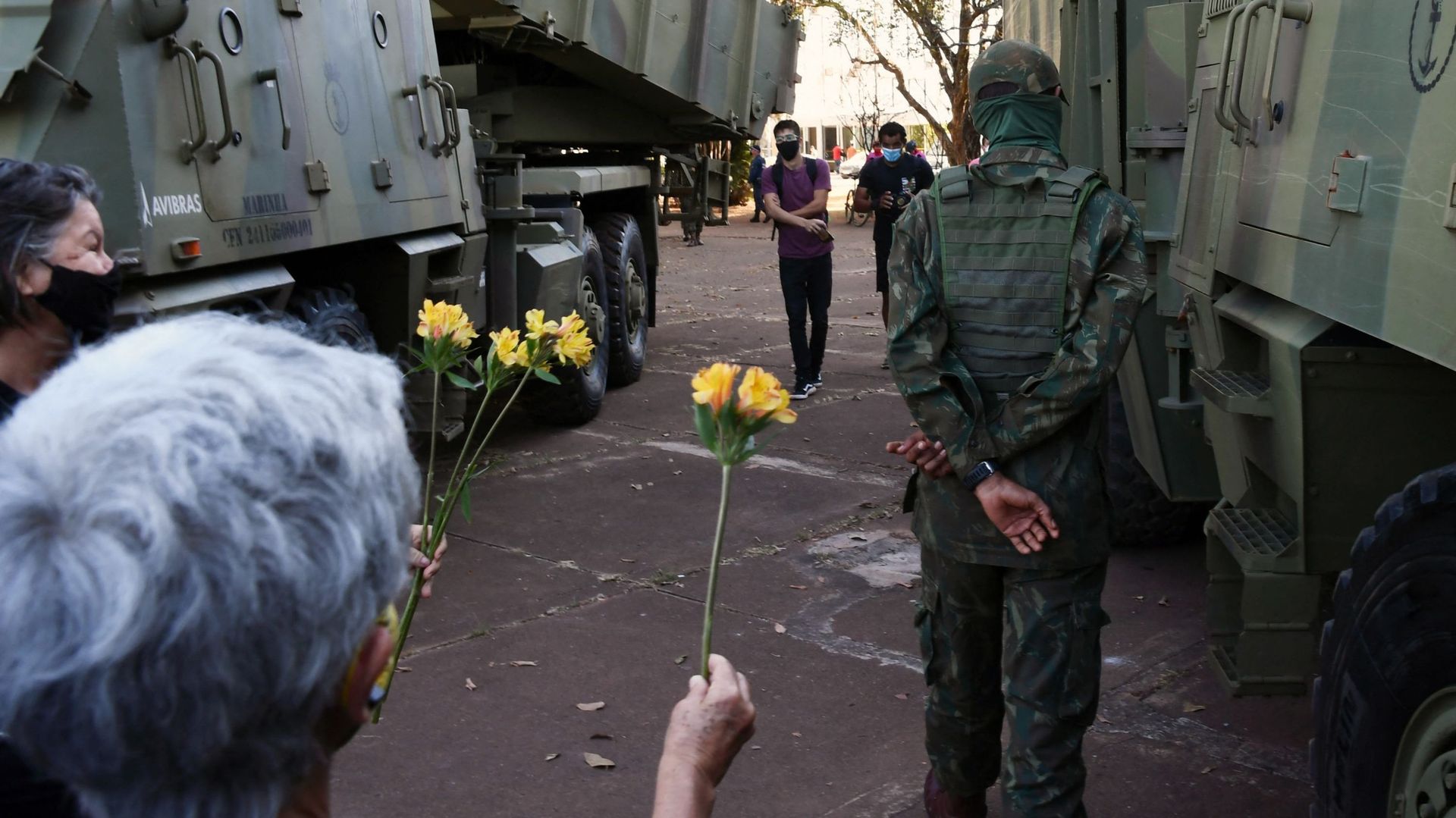 Des manifestants contre un défilé de véhicules militaires devant le palais du Planalto à Brasilia, offrent des fleurs à un soldat ce 10 août 2021. 