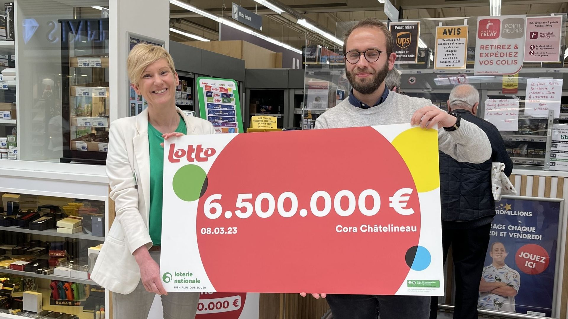 La responsable de la loterie nationale remet le chèque symbolique de 6,5 millions d'euros au responsable marketing du Cora de Châtelineau où le billet du gagnant a été validé.