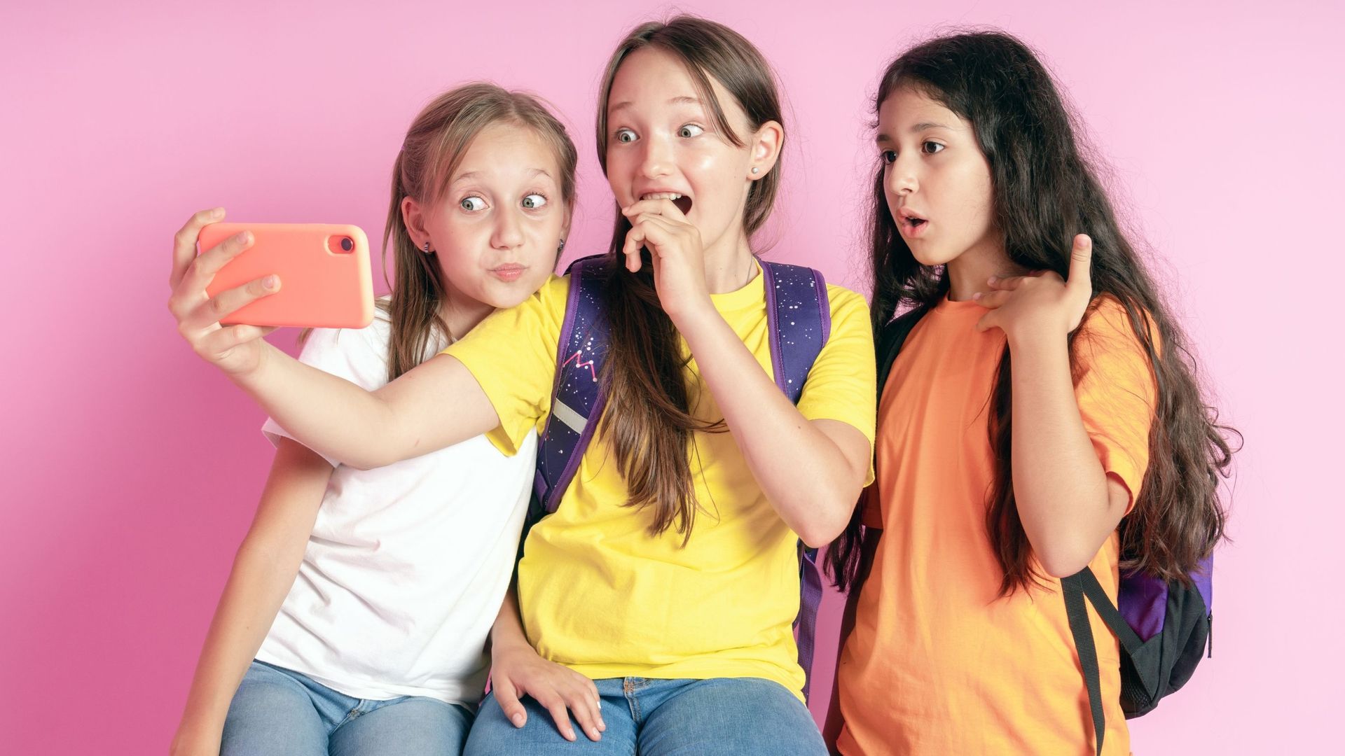 Three teen girls smiling and shoots a video on a pink background. Selfies. Tiktok blogger.
