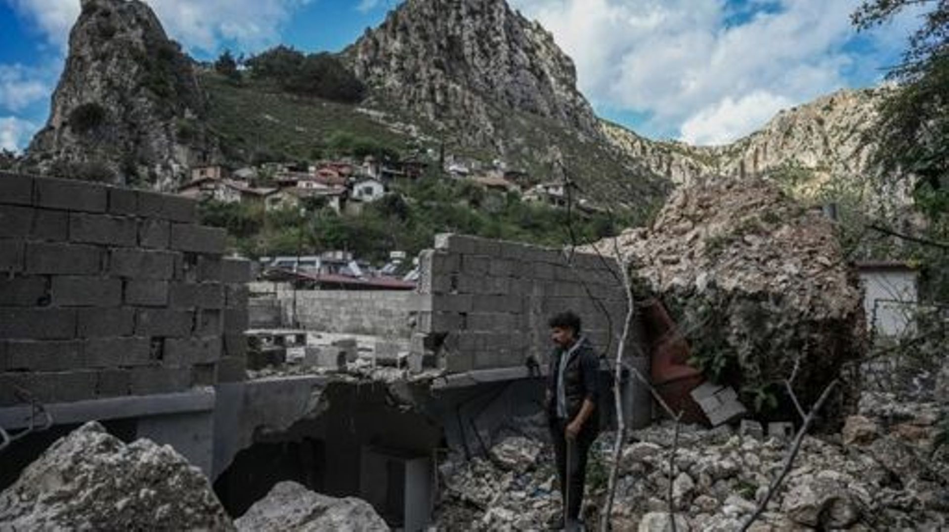 Cuma Zobi (L), a 38-year-old security guard, stands next to a building destroyed by falling stones of the Staurin mountain, two months after a 7.8-magnitude jolt and its aftershocks wiped out swathes of Turkey's mountainous southeast, in Antakya on April 