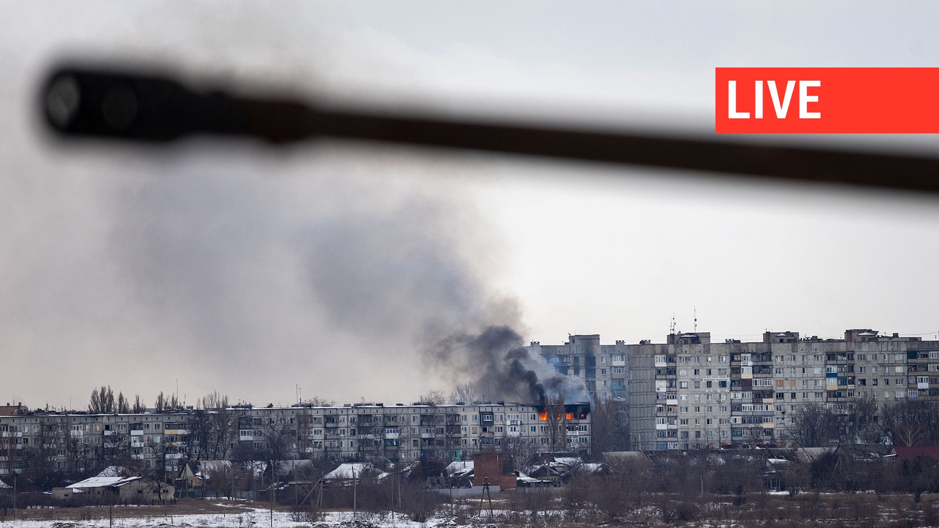 Un véhicule militaire ukrainien passe alors qu'un immeuble d'habitation touché par l'artillerie russe brûle au loin, le 14 février 2023 à Bakhmut, en Ukraine.