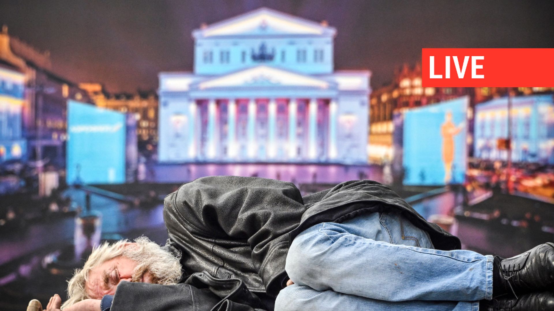 Un homme dort sur un banc devant une affiche représentant le célèbre théâtre Bolchoï de Moscou, le 16 mai 2023.