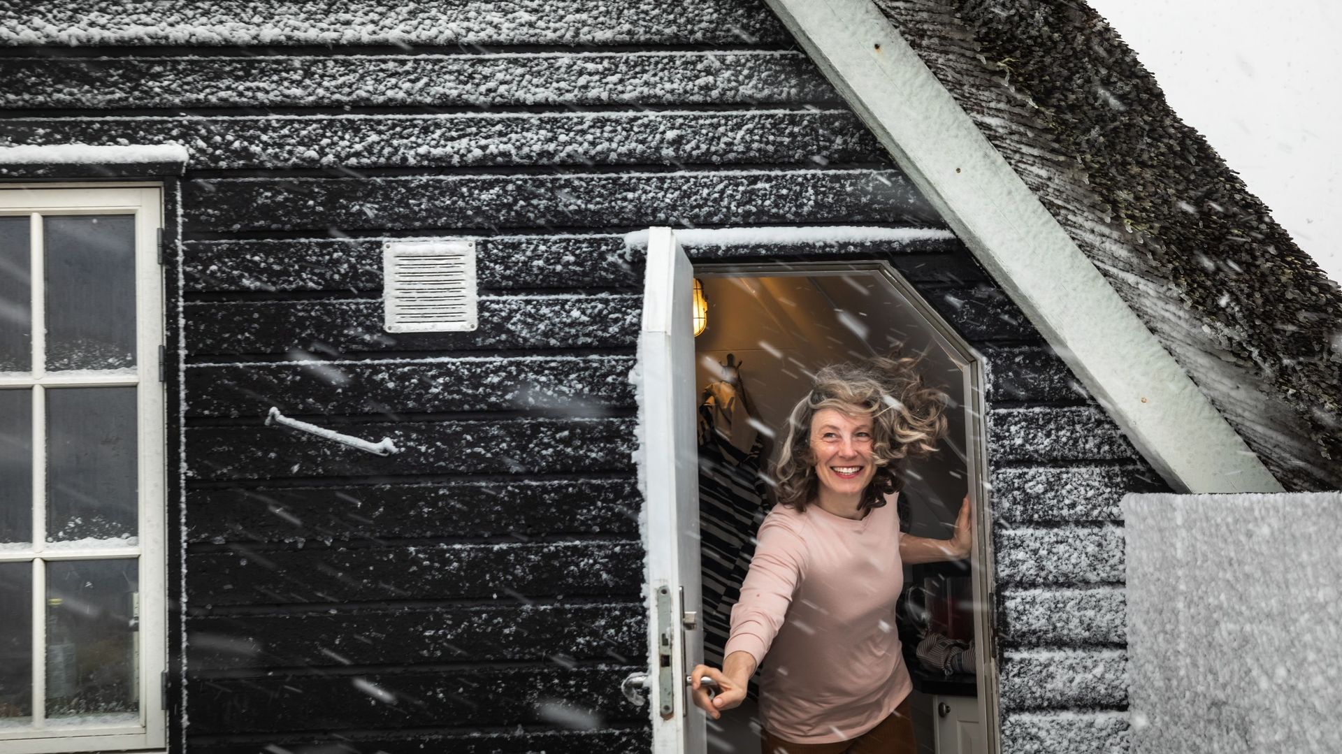 Woman Holding Door Open With Hair Blowing In Snow Storm in Denmark