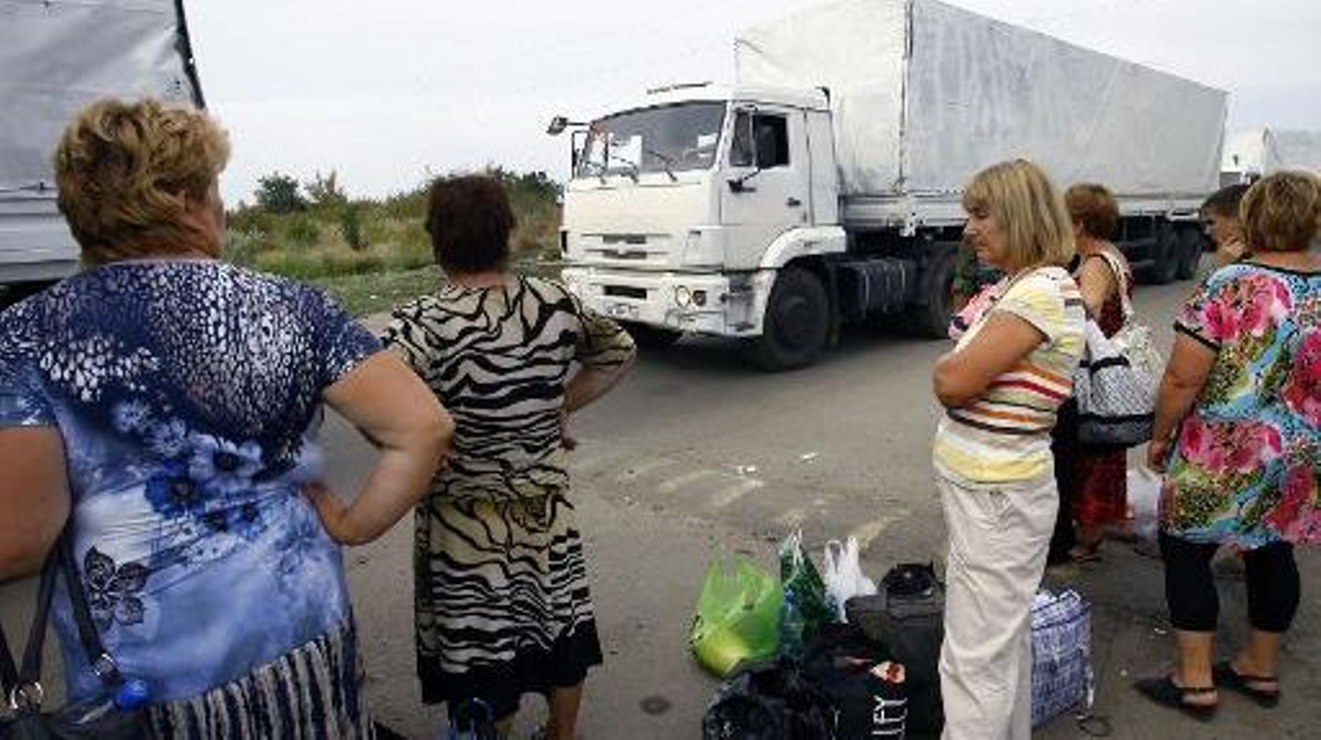 Des femmes observent les camions du convoi humanitaire envoyé par Moscou, au poste frontière d'Izvarino, entre la Russie et l'Ukraine, le 22 août 2014