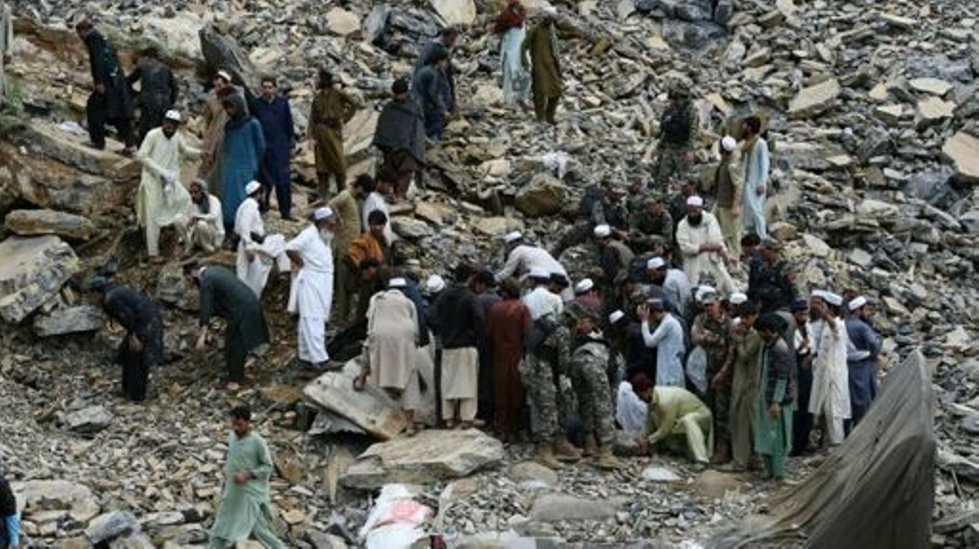 Security officials and onlookers gather near wrecked trucks following a landside near Pakistan’s Torkham border town on April 18, 2023. At least two people were killed and eight injured in a massive pre-dawn landslide that buried dozens of trucks waiting