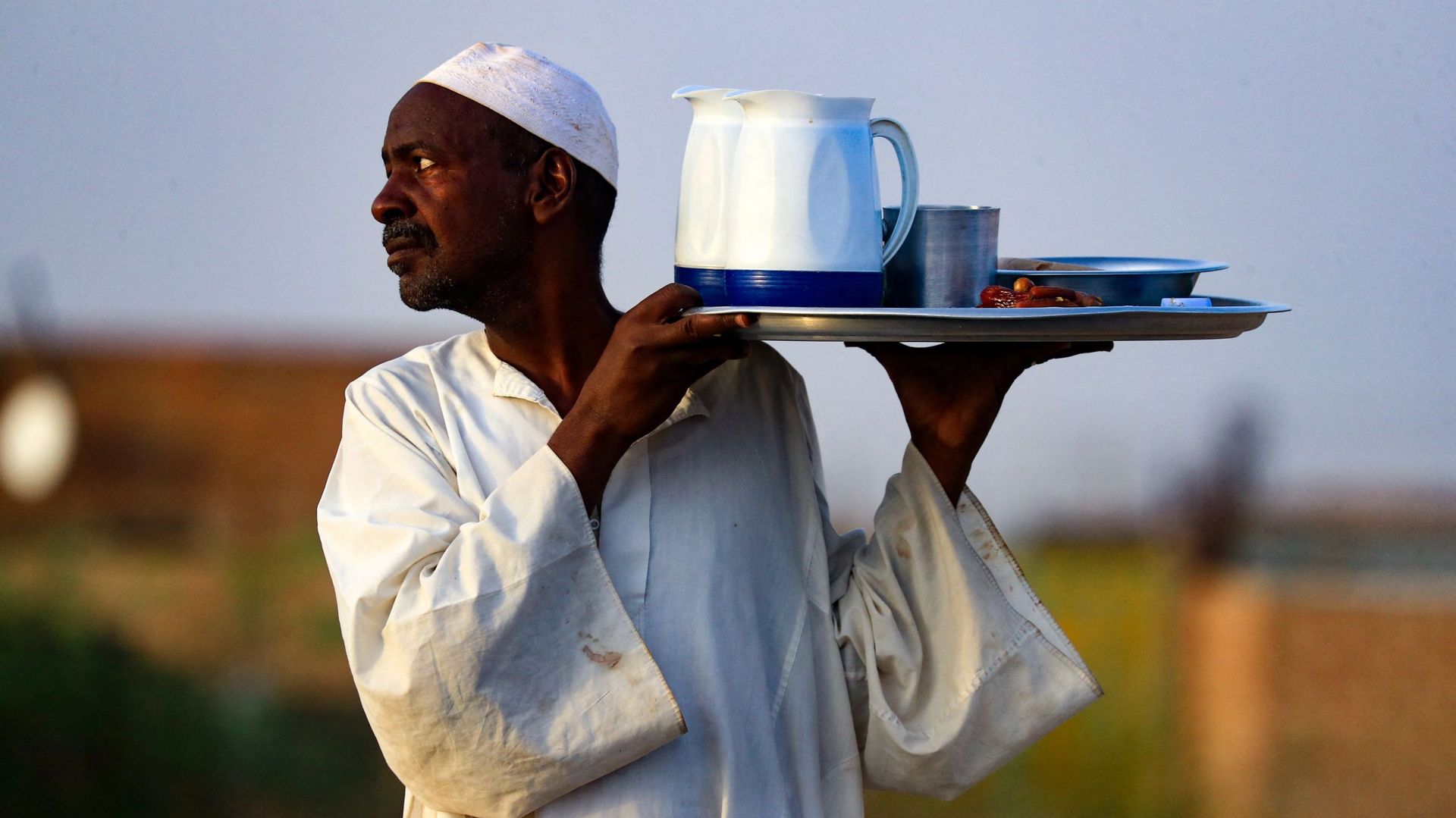 Un homme sert de la nourriture et des boissons lors d’un repas collectif Iftar devant une mosquée le long de la route nationale Jazeera dans le village d’al-Nuba, à environ 50 kilomètres au sud de la capitale du Soudan, le 8 avril 2022, pendant le mois sa