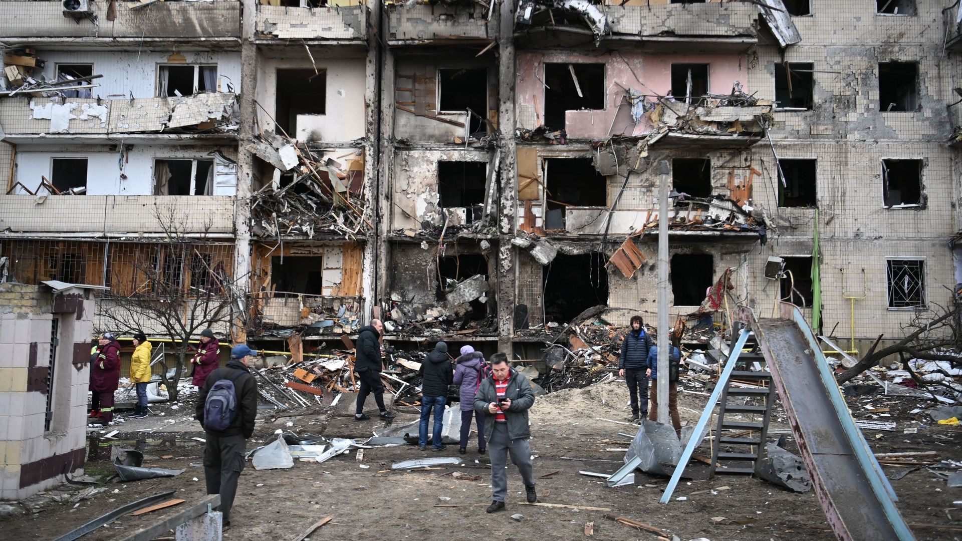 Des personnes se rassemblent devant un bâtiment résidentiel endommagé dans la rue Koshytsa, une banlieue de la capitale ukrainienne Kiev, où un obus militaire aurait frappé, le 25 février 2022.