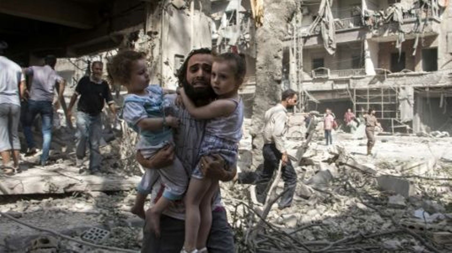 Un homme porte ses deux filles dans les décombres d'immeubles après une attaque aux barils d'explosifs, le 17 septembre 2015 à Alep