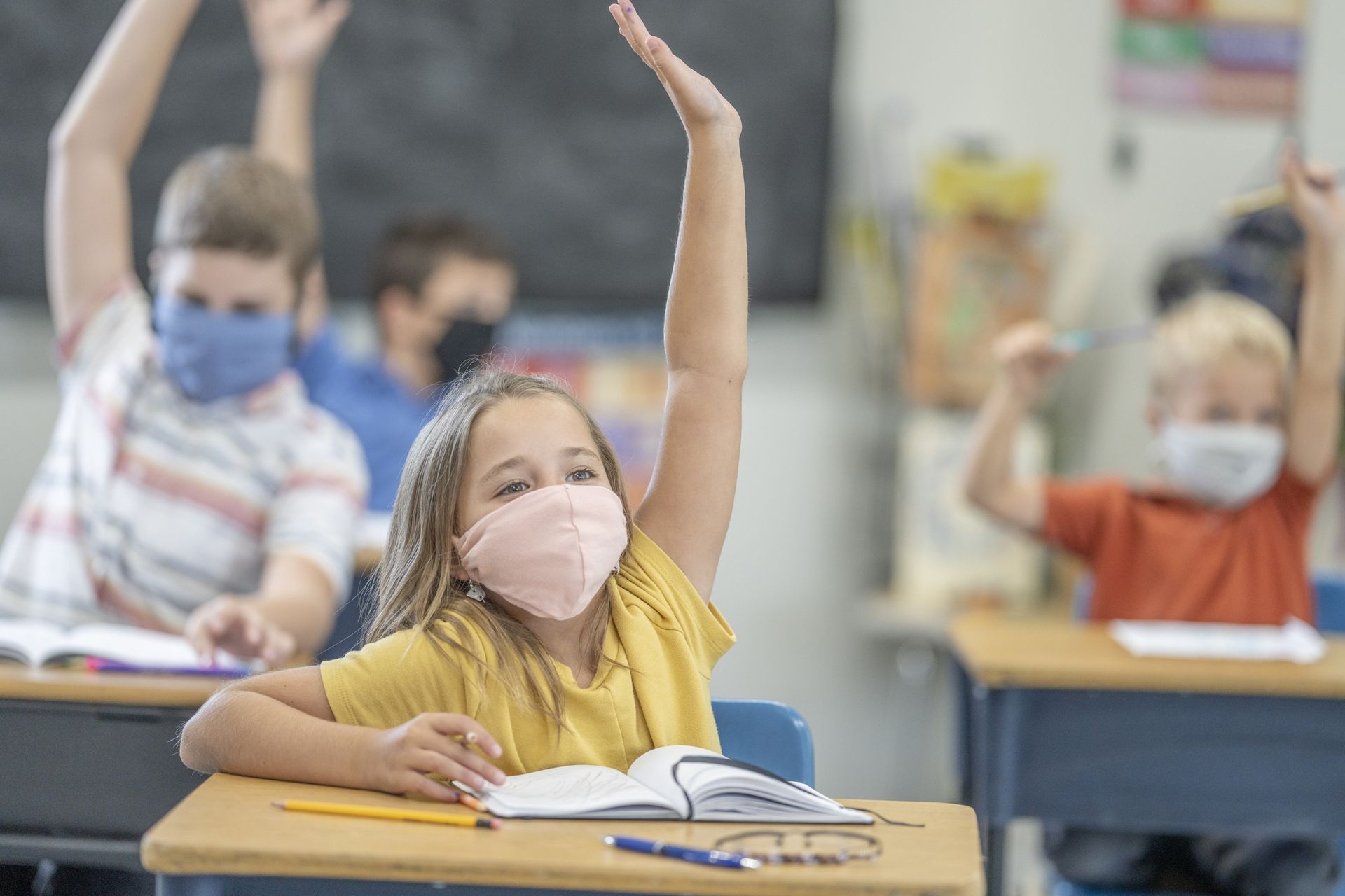 Illustration. Groupe d’élèves portant des masques de protection tout en levant la main en classe.