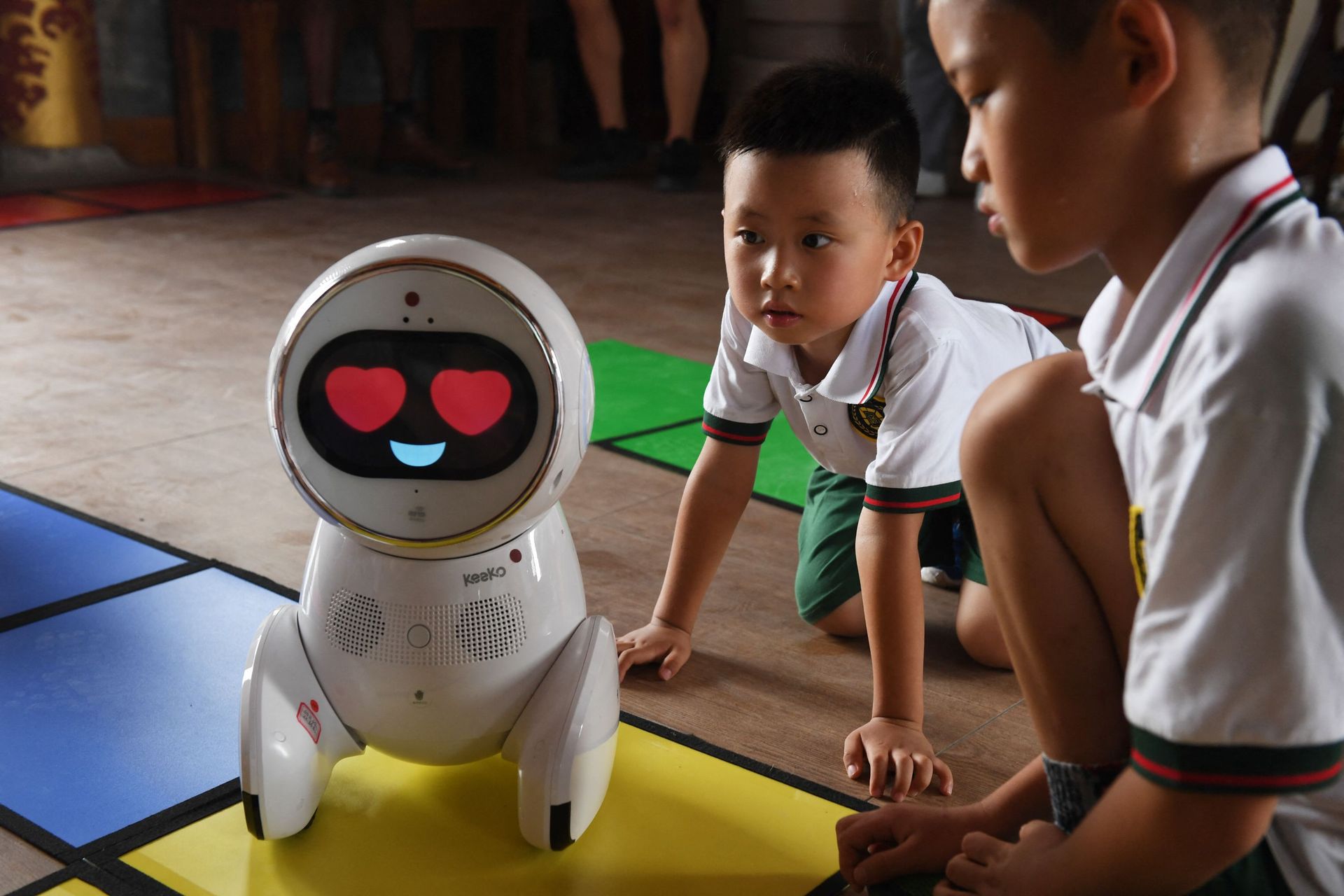 Cette photo prise le 30 juillet 2018 montre des enfants regardant un robot Keeko se frayer un chemin sur un sentier qu'ils ont fabriqué avec des tapis carrés à l'Institut Yiswind d'éducation multiculturelle à Pékin.